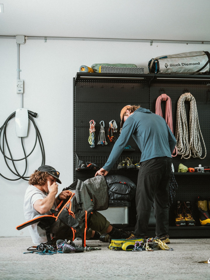 Two people preparing outdoor equipment beside a PegGrid wall displaying climbing ropes, bags and accessories.