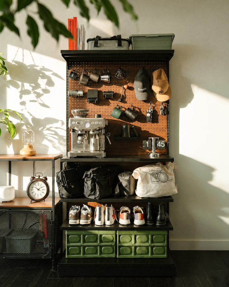 A PegGrid coffee station with an espresso machine, hanging mugs, bags and storage crates in warm window light.