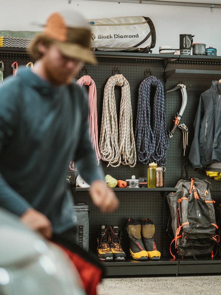 A person moves past a PegGrid wall displaying climbing ropes, jackets, boots and outdoor bags.