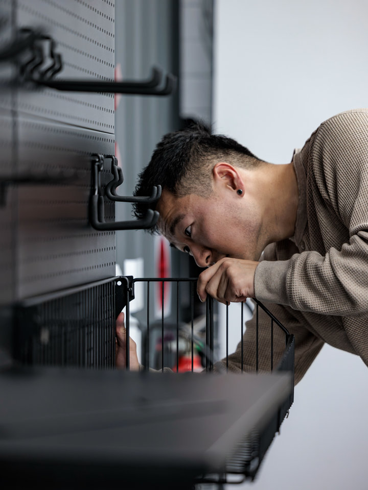 A close view of a person adjusting a wire storage basket on a dark PegGrid panel.