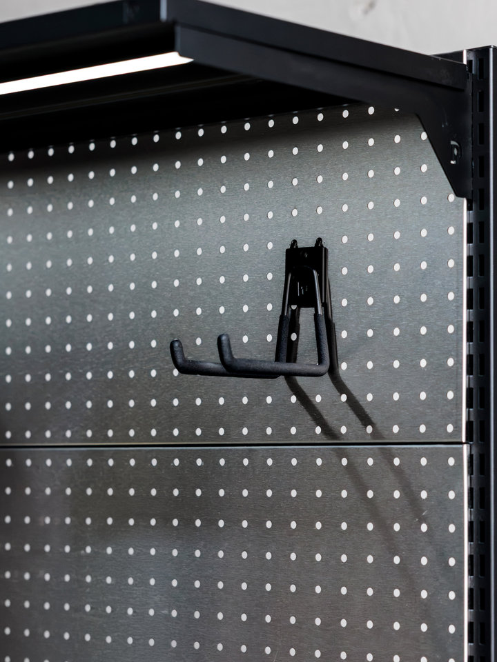 A black storage hook mounted on a metal PegGrid panel beneath a shelf.