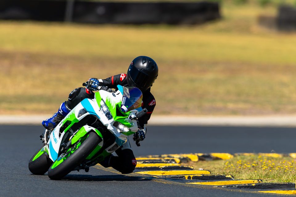 A rider on a green sports motorcycle approaching a track corner in daylight