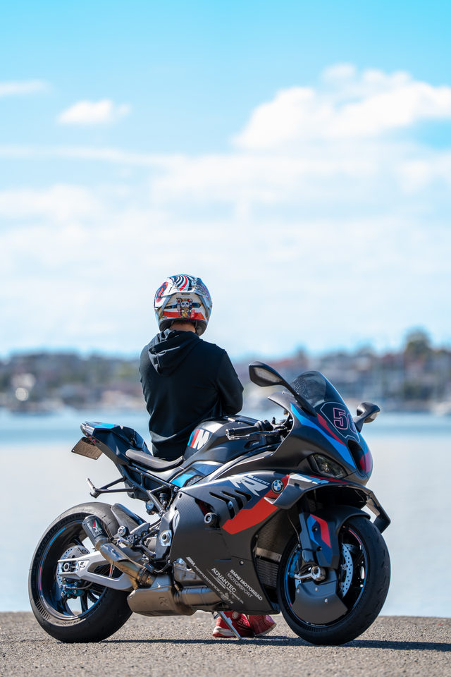 A helmeted rider with a sports motorcycle beside the water