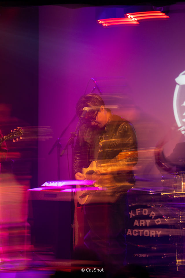 A musician rendered with intentional motion blur in magenta stage light