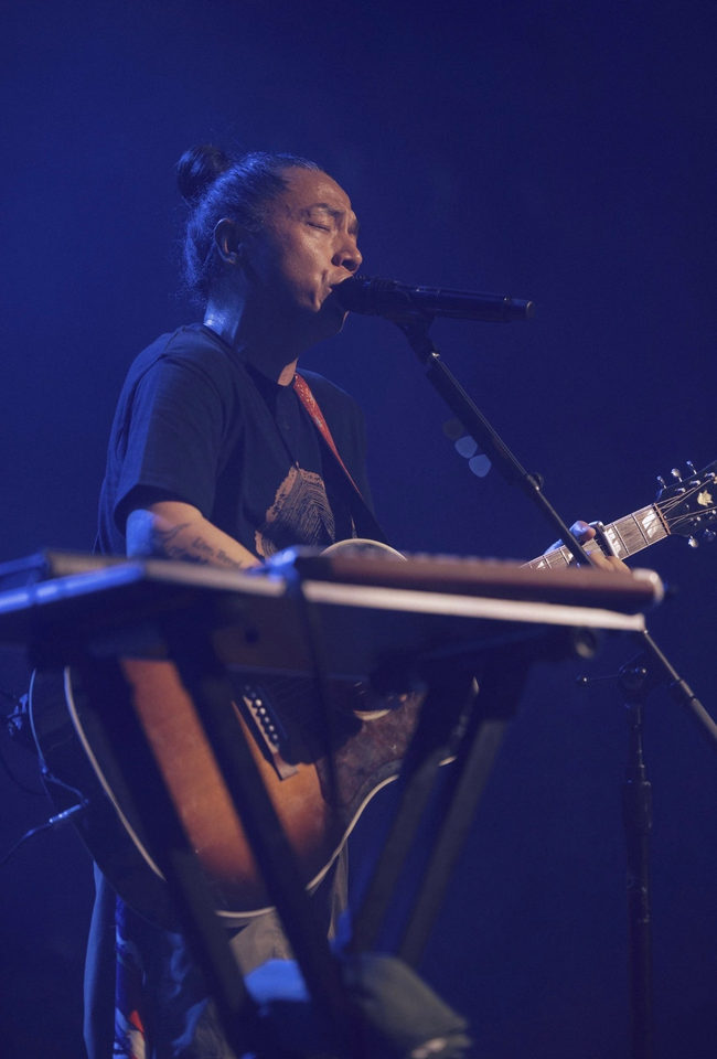 A performer singing beside a keyboard under blue stage lighting